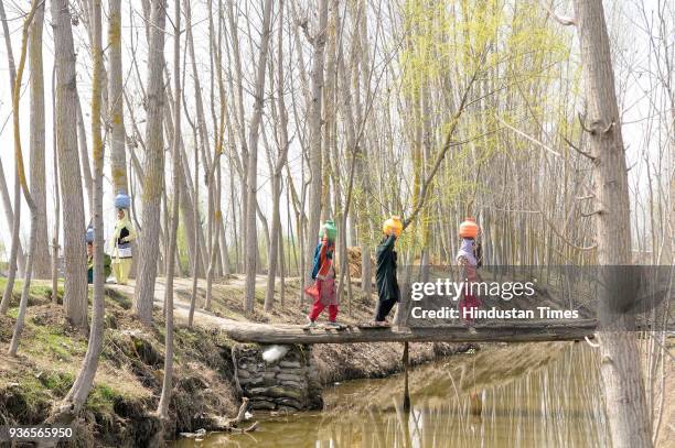 Kashmiri girls carry a water container after filling them with water from a nearby stream at Dasilpora village of Pattan, North Kashmir, on March 22,...