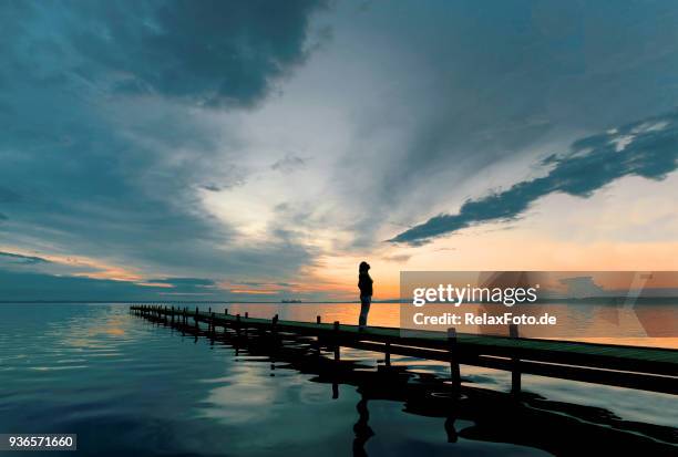 silhouette der frau auf see anlegestelle in abenddämmerung beobachten majestätische wolkengebilde - bootssteg stock-fotos und bilder