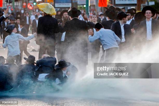 Members of the Israeli security forces spray water as they try to disperse ultra-Orthodox Jews from blocking the road in a demonstration against...