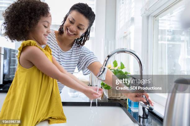 mom helps young daughter wash hands - kitchen sink running water stock pictures, royalty-free photos & images