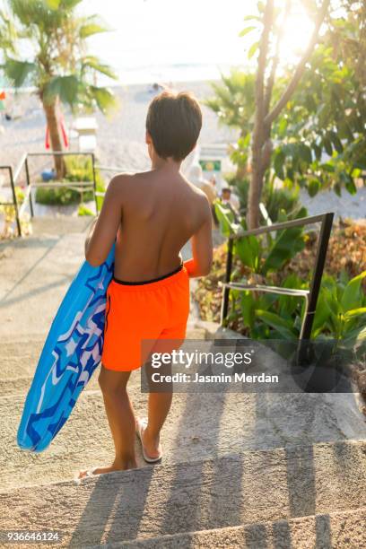 young teenage boy walking with inflatable lounger - teen boy barefoot stock pictures, royalty-free photos & images