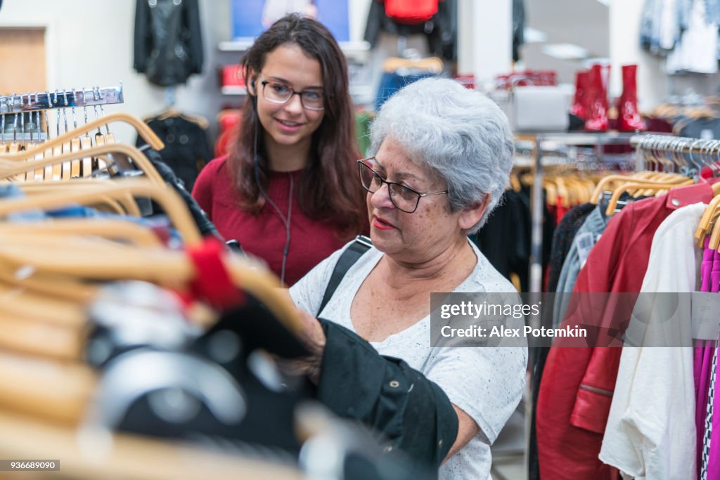 The silver-haired 65-years-old active senior woman and her teenager granddaughter shopping in the clothing retail store