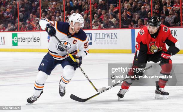 Connor McDavid of the Edmonton Oilers chips the puck past Cody Ceci of the Ottawa Senators in the first period at Canadian Tire Centre on March 22,...