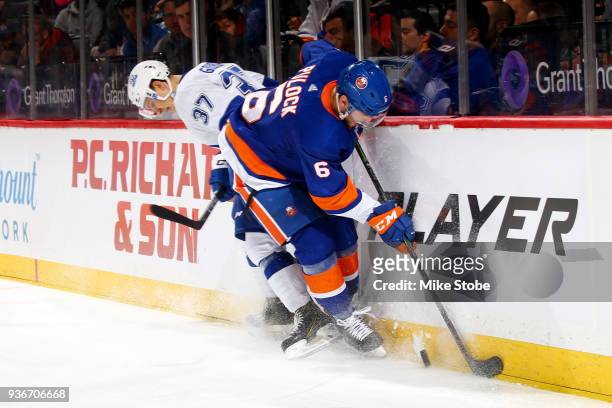 Ryan Pulock of the New York Islanders and Yanni Gourde of the Tampa Bay Lightning battle for the puck along the boards at Barclays Center on March...