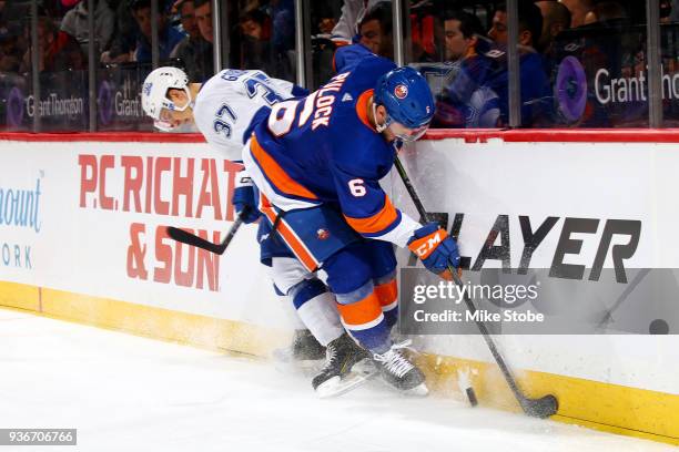 Ryan Pulock of the New York Islanders and Yanni Gourde of the Tampa Bay Lightning battle for the puck along the boards at Barclays Center on March...