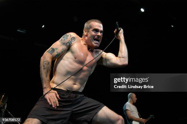 Rollins Band at Nokia Theater. Henry Rollins, grimacing, raises his left fist with mic to pause as he sings in performance with Rollins Band on June...