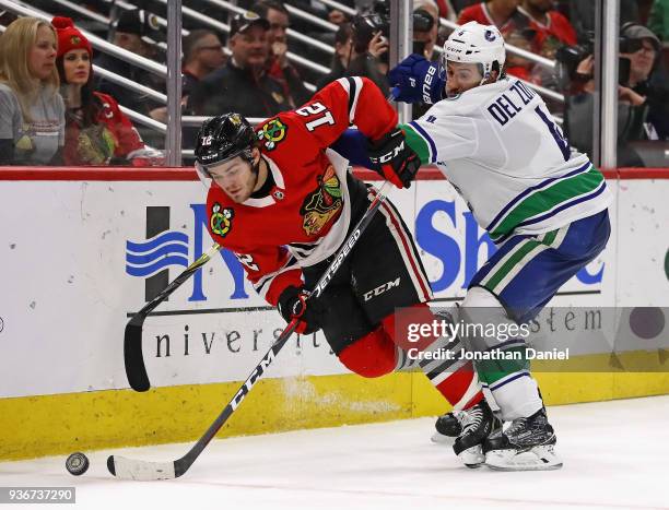 Michael Del Zotto of the Vancouver Canucks shoves Alex DeBrincat of the Chicago Blackhawks to the ice at the United Center on March 22, 2018 in...