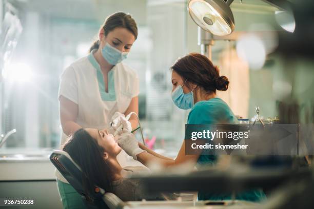 dentist and her assistant performing dental drilling on young woman. - dental drill stock pictures, royalty-free photos & images