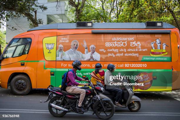 Motorcyclists ride past a bus featuring an image of Indian Prime Minister Narendra Modi parked outside the Bharatiya Janata Party office in...