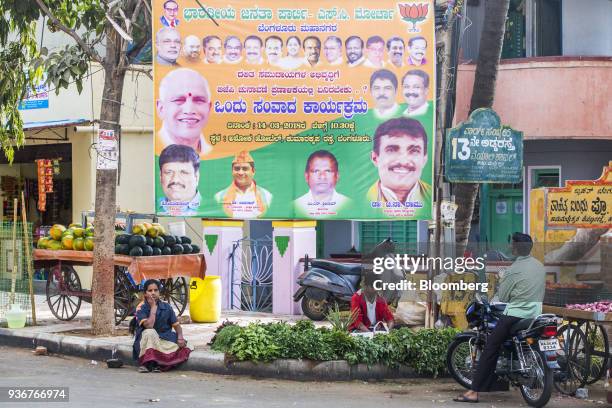 Vendor sits in front of a vegetables stall near an election campaign billboard for the Bharatiya Janata Party in Bengaluru, Karnataka, India, on...