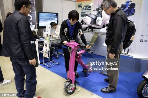 An attendant, center, demonstrates an Access Co. Cute-mL electric vehicle to attendees at the Tokyo Motorcycle Show in Tokyo, Japan, on Friday, March...