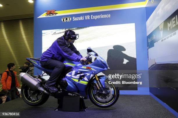 An attendant wearing a virtual reality headset rides a Suzuki Motor Corp. GSX-R1000R motorcycle during a driving simulation at the Tokyo Motorcycle...