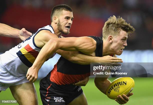 Joshua Begley of the Bombers handballs whilst being tackled during the round one AFL match between the Essendon Bombers and the Adelaide Crows at...