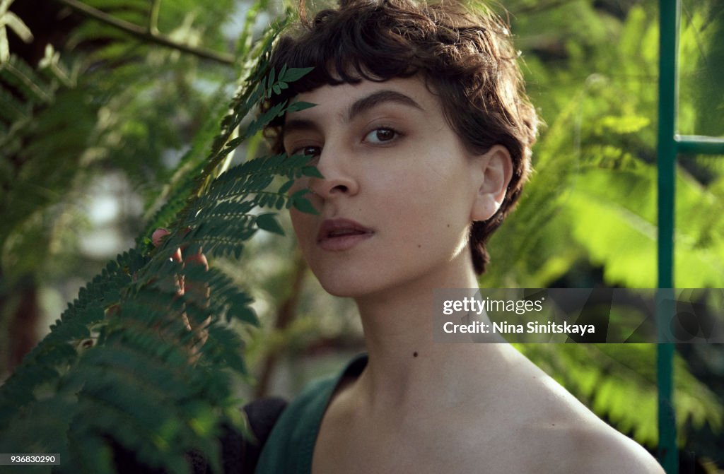 Beautiful woman face behind palm tree leaf on sunset time