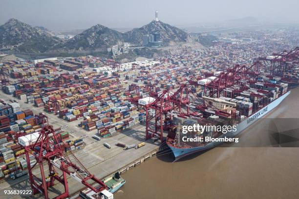 An A.P. Moller-Maersk A/S container ship is docked as shipping containers stand in a terminal at the Yangshan Deep Water Port in this aerial...