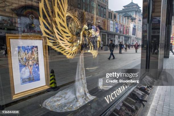 Pedestrians and shoppers are reflected in the window of a Victoria's Secret Stores LLC store on Wangfujing Street in Beijing, China, on Friday, March...