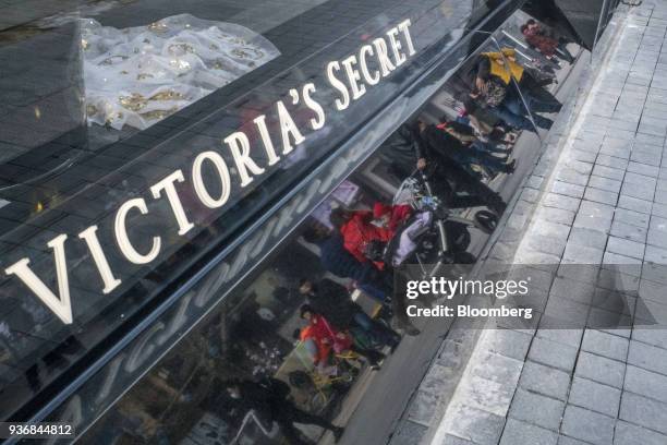 Pedestrians and shoppers are reflected in a Victoria's Secret Stores LLC store on Wangfujing Street in Beijing, China, on Friday, March 23, 2018. The...