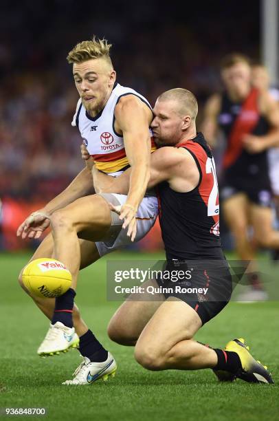Hugh Greenwood of the Crows kicks whilst being tackled by Jake Stringer of the Bombers during the round one AFL match between the Essendon Bombers...
