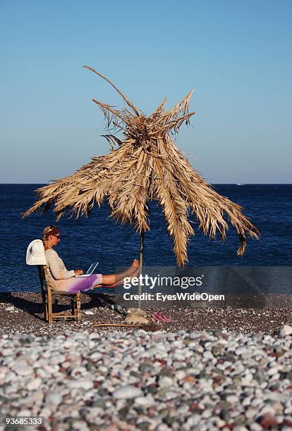 Woman on a beach working with a notebook near Lindos on July 16, 2009 in Rhodes, Greece. Rhodes is the largest of the Greek Dodecanes Islands.