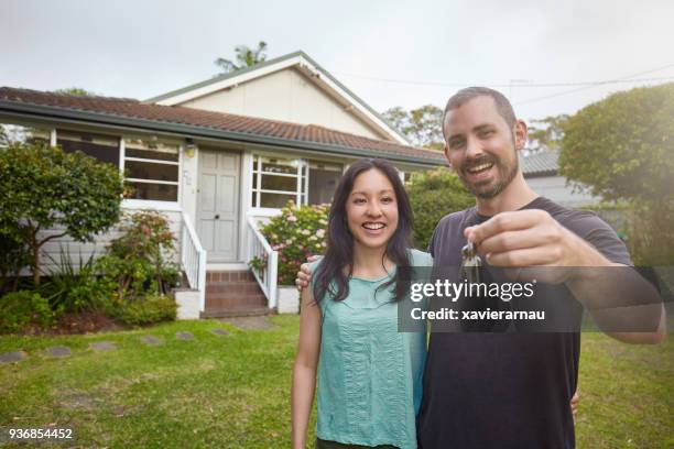 happy mixed-race couple showing the keys of the new house - moving house stock pictures, royalty-free photos & images