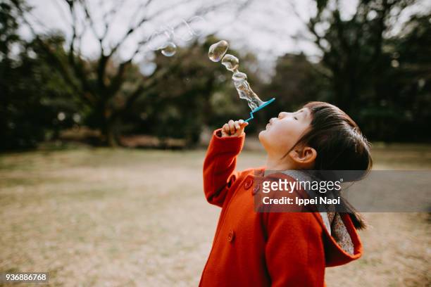 adorable little girl in red coat blowing bubbles in park - child bubble stock-fotos und bilder
