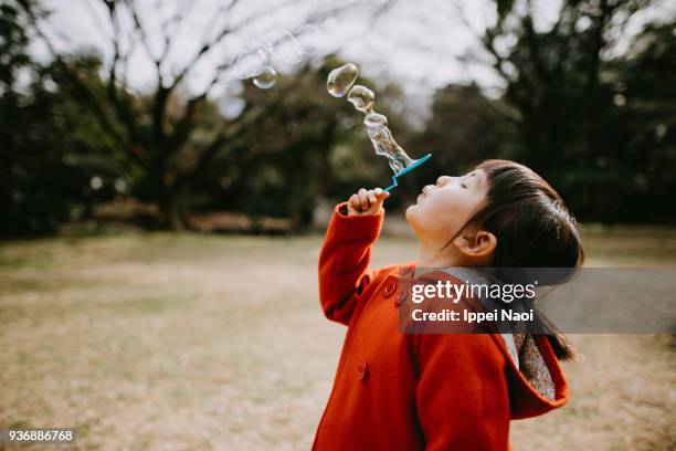 adorable little girl in red coat blowing bubbles in park - season 3 stockfoto's en -beelden