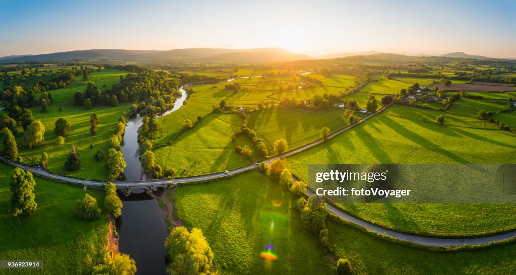 Aerial panorama over idyllic countryside green fields mountains golden sunset
