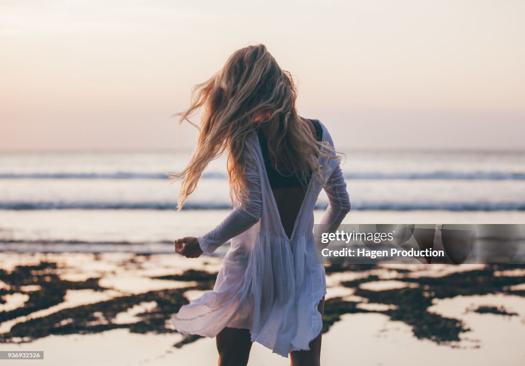 Beautiful blonde girl with long hair in short white dress dancing at sunset