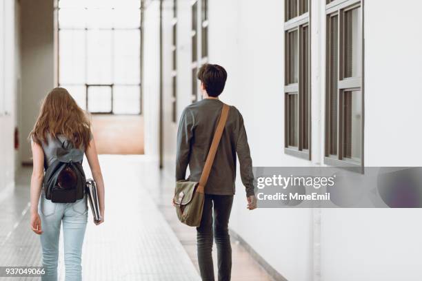 dos adolescentes caminando en el pasillo en la escuela. vista trasera. un muchacho y una muchacha - boy and girl talking fotografías e imágenes de stock