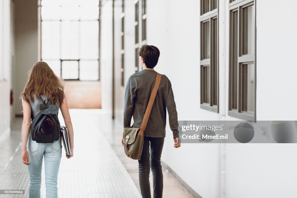 Two teenagers walking in the corridor at school. Rear view. One boy and one girl