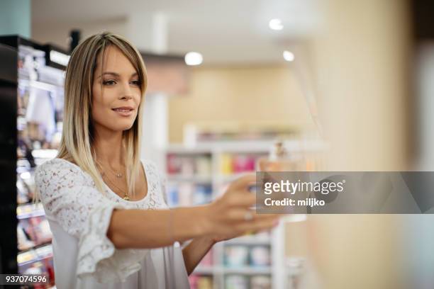 young woman shopping at cosmetics and make-up shop - choosing perfume stock pictures, royalty-free photos & images