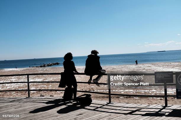 People look out at the water along the Coney Island boardwalk on a spring afternoon on March 23, 2018 in New York City. Following weeks of cold, snow...