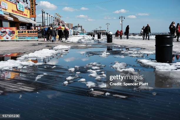 People walk by puddles from snow melt along the Coney Island boardwalk on a spring afternoon on March 23, 2018 in New York City. Following weeks of...