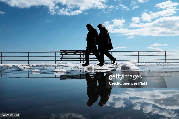 Couple walks by puddles from snow melt along the Coney Island boardwalk on a spring afternoon on March 23, 2018 in New York City. Following weeks of...