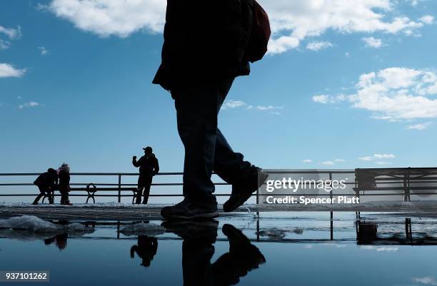 People walk by puddles from snow melt along the Coney Island boardwalk on a spring afternoon on March 23, 2018 in New York City. Following weeks of...