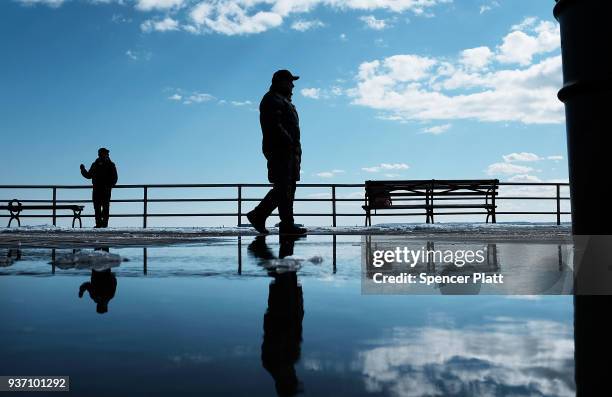 People walk by puddles from snow melt along the Coney Island boardwalk on a spring afternoon on March 23, 2018 in New York City. Following weeks of...
