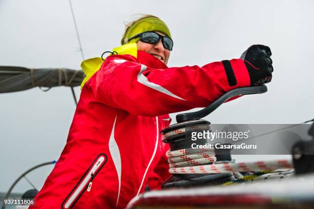frau in rot jacke ziehen das seil mit hilfe einer winde auf kurs segeln - kabelwinden stock-fotos und bilder