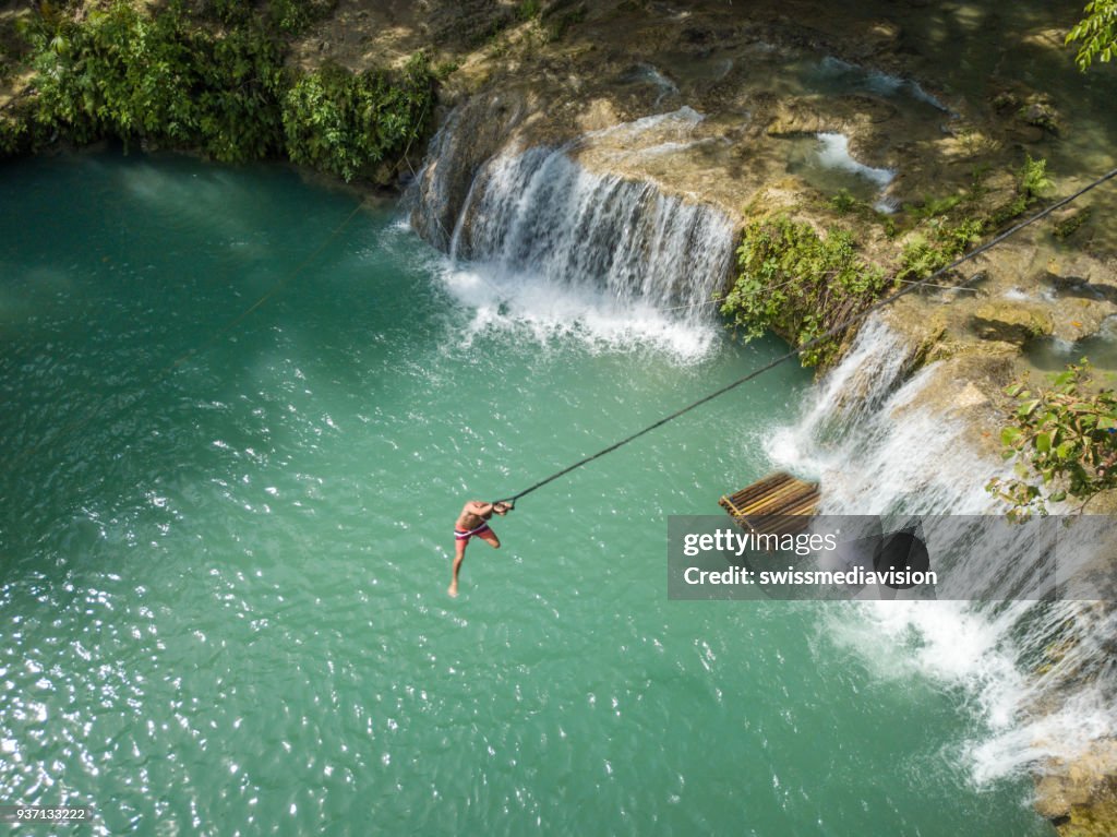 Drone point of view of man jumping into waterfall pool