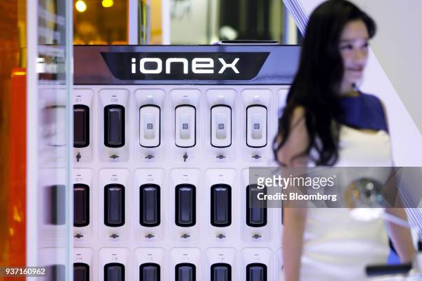 An attendee stands in front of Kwang Yang Motor Co. Ionex battery packs charging inside an Ionex energy station on display at the Tokyo Motorcycle...