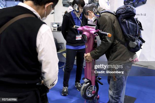 An attendee, left, lifts a folded Access Co. Cute-mL electric vehicle at the Tokyo Motorcycle Show in Tokyo, Japan, on Friday, March 23, 2018. The...