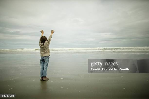 boy stands at beach with arms outstretched - kids standing stock-fotos und bilder