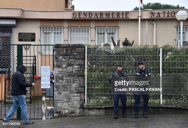 Man prepares to lay a flower as two gendarmes stand guard in front of the Gendarmerie Nationale in Carcassonne on March 24, 2018 in tribute to a...