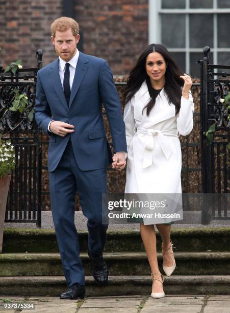 Prince Harry and Meghan Markle, wearing a white belted coat by Canadian brand Line The Label, attend a photocall in the Sunken Gardens at Kensington...