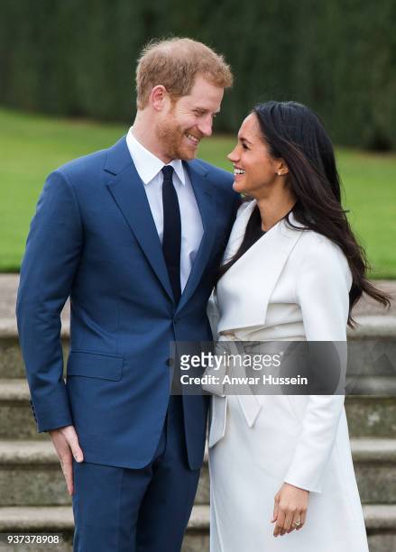 Prince Harry and Meghan Markle, wearing a white belted coat by Canadian brand Line The Label, attend a photocall in the Sunken Gardens at Kensington...
