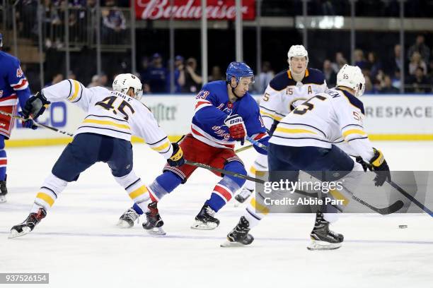 Kevin Hayes of the New York Rangers reaches for the puck against Brendan Guhle and Rasmus Ristolainen of the Buffalo Sabres in the second period...