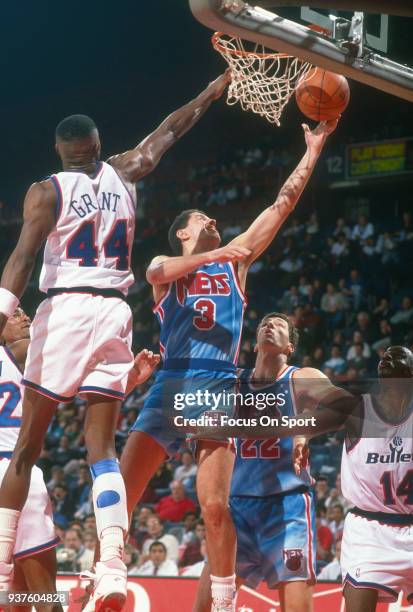 Drazen Petrovic of the New Jersey Nets goes in for a layup over Harvey Grant of the Washington Bullets during an NBA basketball game circa 1991 at...