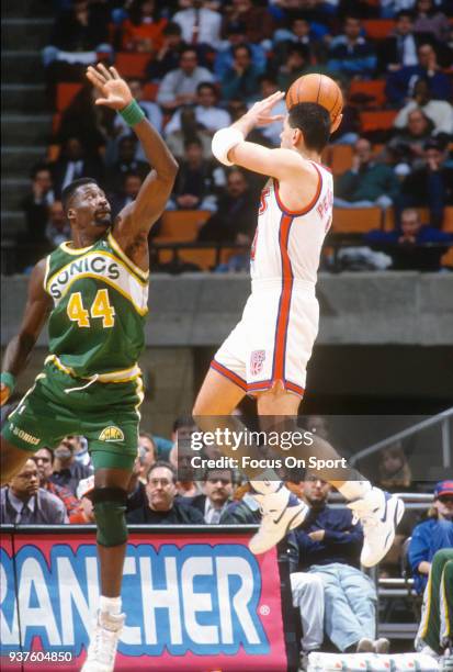 Drazen Petrovic of the New Jersey Nets leaps in the air to pass the ball over Michael Cage of the Seattle Supersonics during an NBA basketball game...