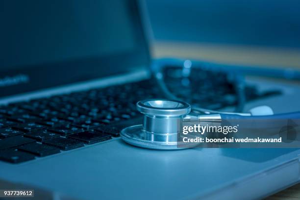 computer or data analysis - stethoscope over a laptop computer keyboard toned in blue - medische artikelen stockfoto's en -beelden
