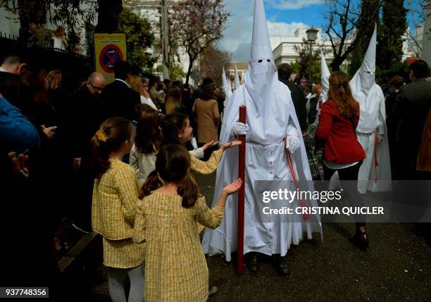 Children ask for candy from a penitent of the 'La Paz' brotherhood takes part in the Palm Sunday procession in Sevilla at the start of the Holy Week...