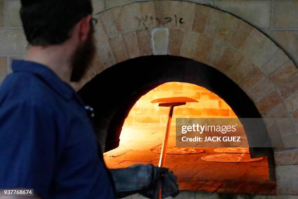 An Ultra-Orthodox Jewish man loads the Matzoth into the oven on March 25, 2018 at a bakery in Kfar Habad near Tel Aviv. - Religious Jews throughout...